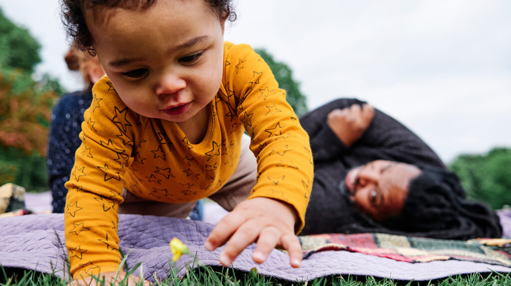 Bebé gateando sobre una manta de picnic, los padres miran