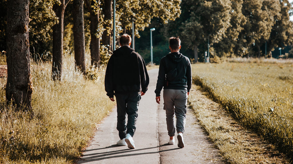 Dos amigos varones caminando por una pequeña carretera al aire libre