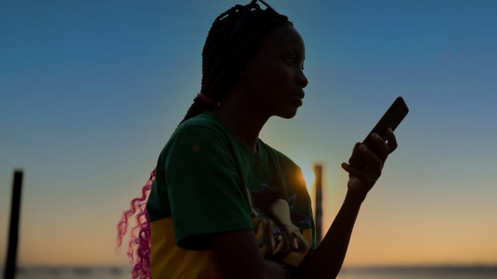 Mujer mirando el teléfono móvil al atardecer junto al mar