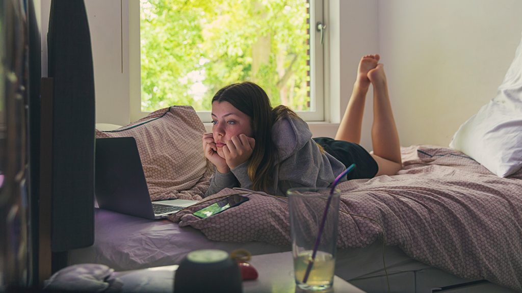 Adolescente en su cama, mirando su computadora