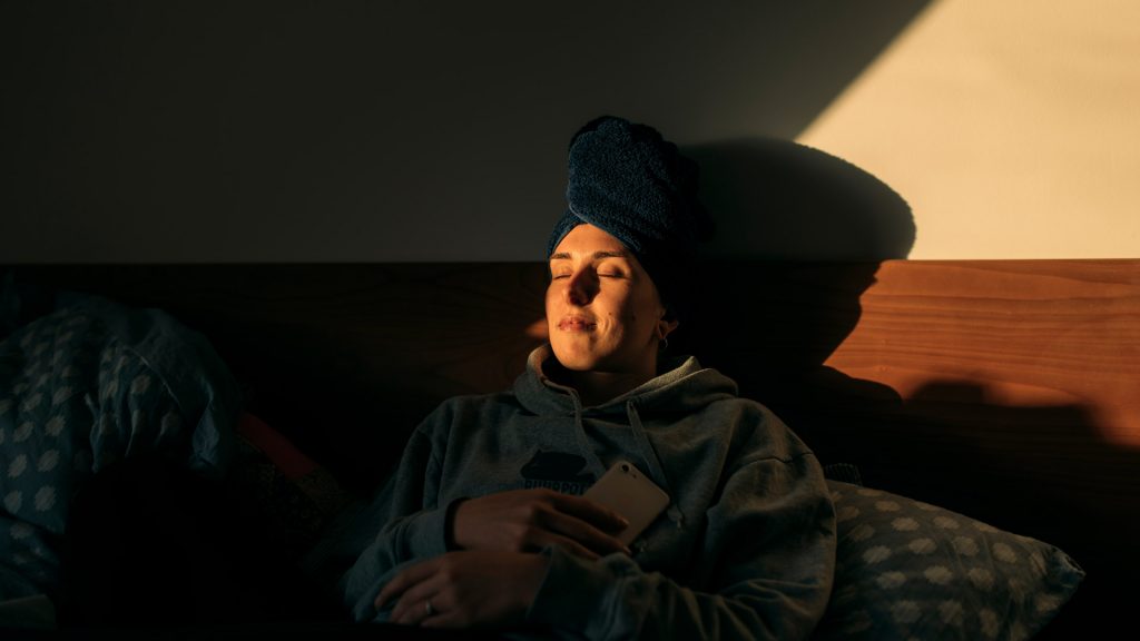 Mujer descansando en la cama con teléfono móvil