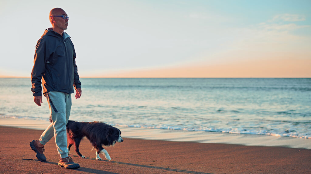 Viejo paseando a un perro en la playa
